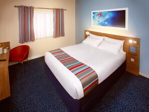 A hotel room with a large bed, a red chair, a desk with a telephone, and a painting on the wall. - Travelodge Sedgefield (Stockton-on-Tees)