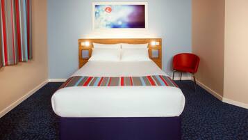 A hotel room with a large bed, a headboard with lights, a red chair, and a painting on the wall.
