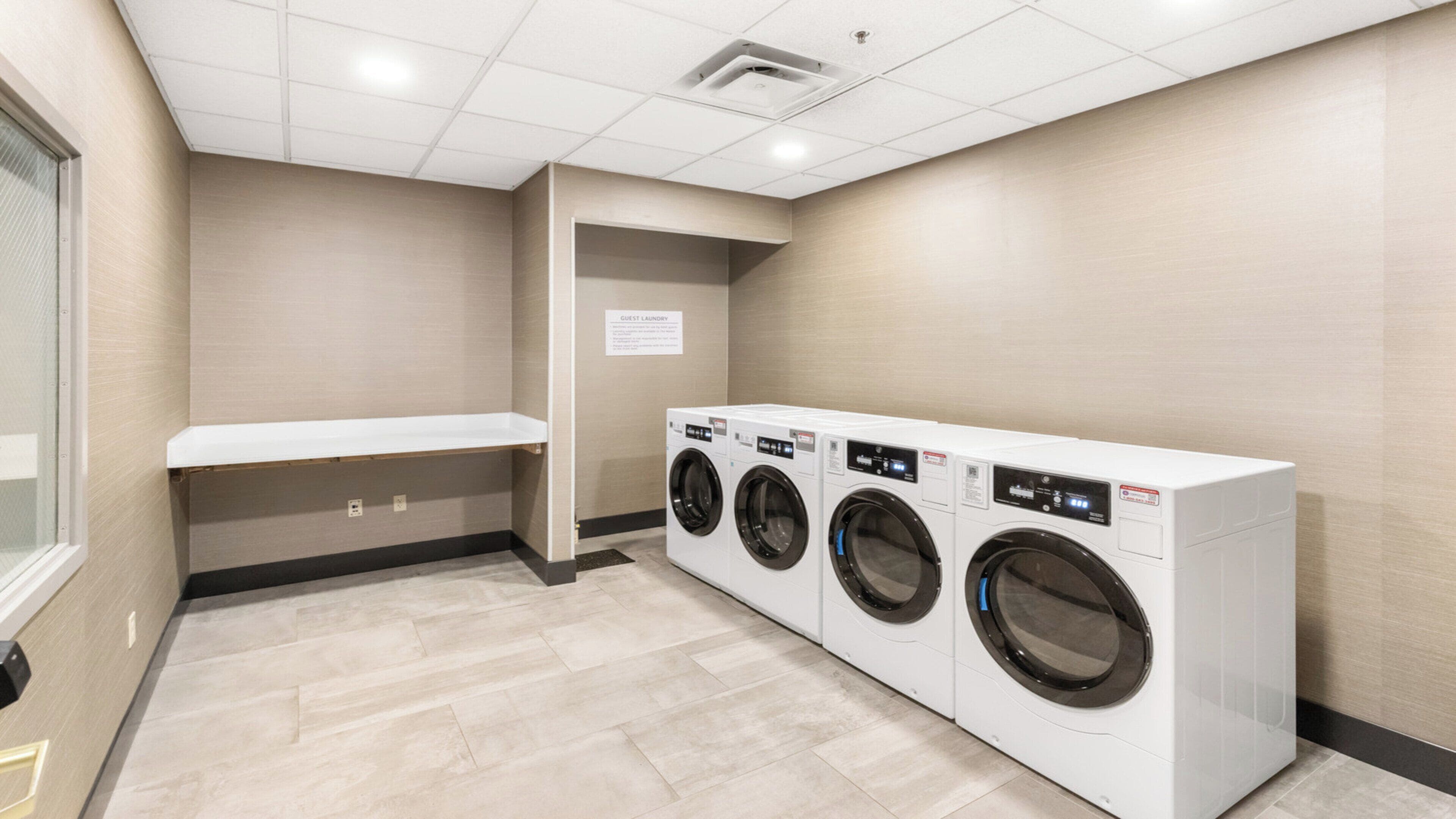 A laundry room with three front-loading washing machines, a bench, and a sign indicating guest laundry.