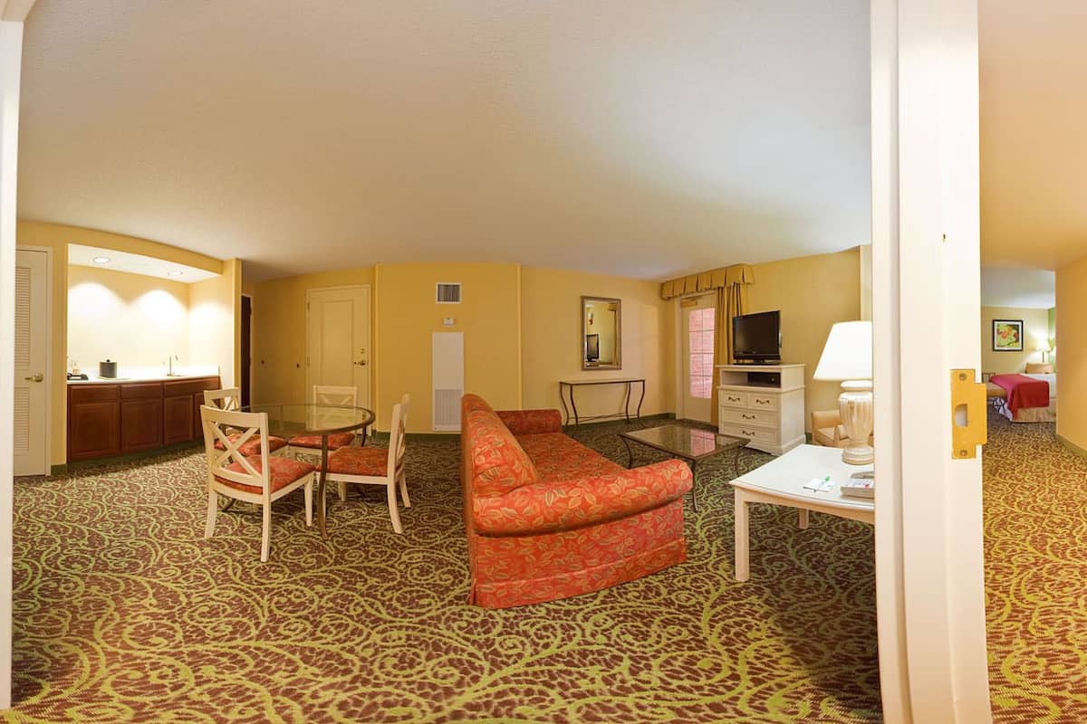 A hotel room with a red sofa, a dining table with chairs, a TV, and a small kitchen area.