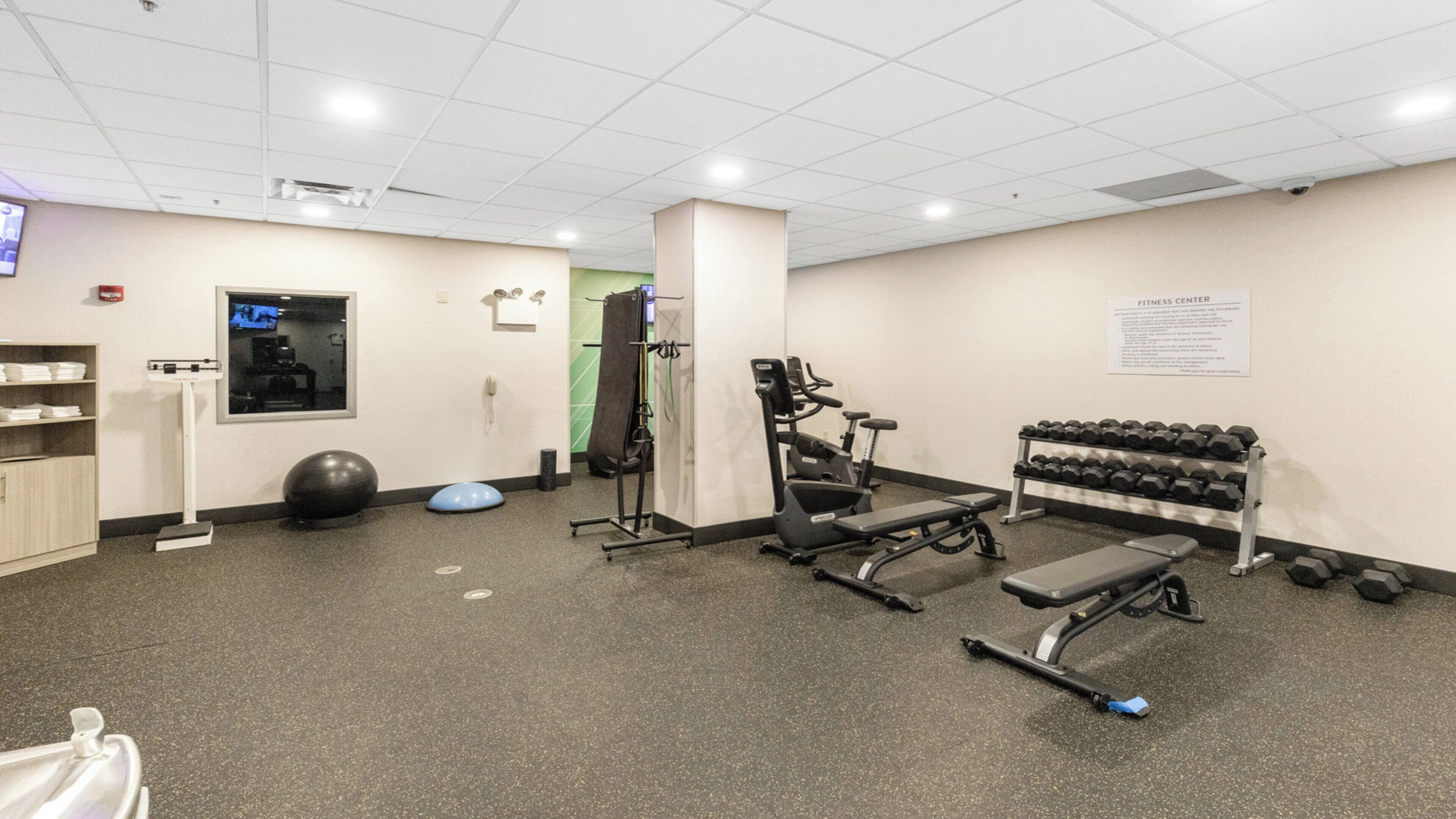 Une salle de sport équipée de matériel d’exercice, d’un téléviseur fixé au mur et d’un porte-haltères.