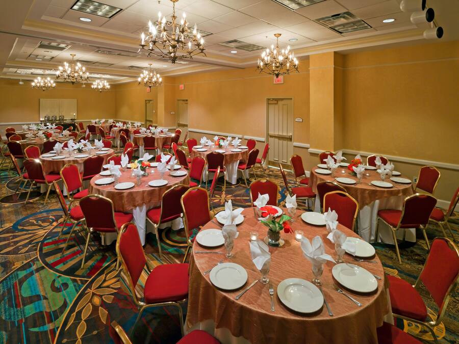 A banquet hall with round tables, red chairs, and chandeliers.
