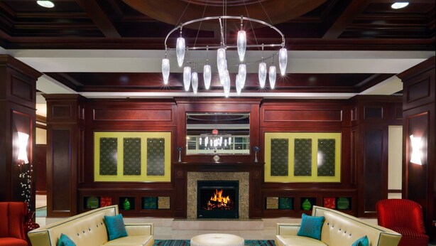 A spacious lobby with a large chandelier, a fireplace, and two sofas with ottomans. - Holiday Inn Chantilly - Dulles Arpt Area by IHG (Chantilly)
