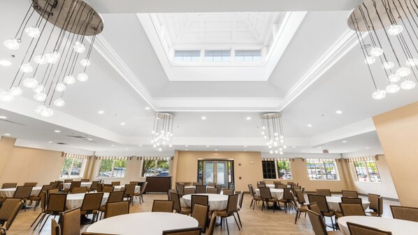 Une salle de conférence spacieuse, dotée de plusieurs tables et chaises, d’une verrière et de luminaires suspendus.