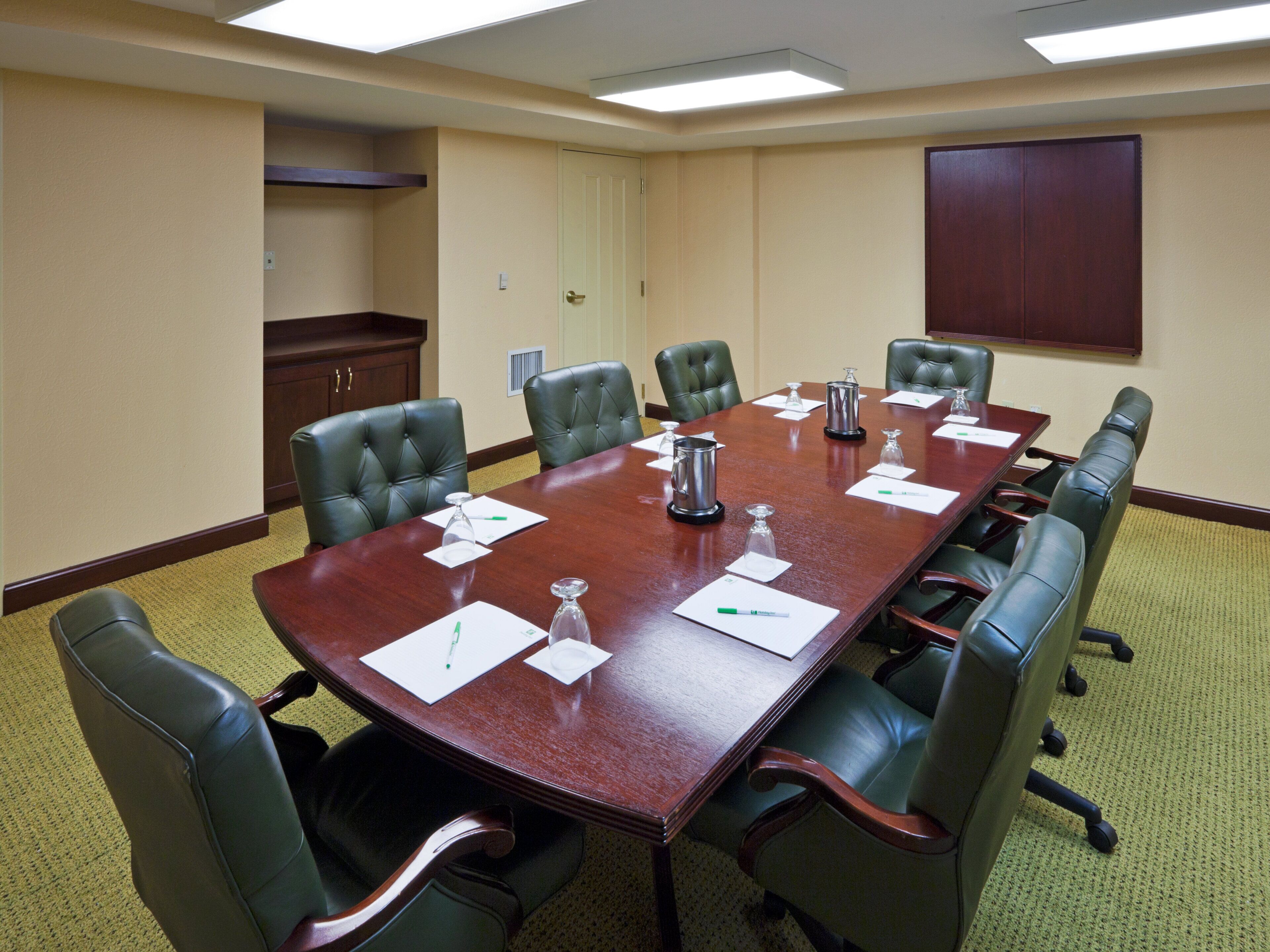 A conference room with a long table, leather chairs, and a wooden cabinet.