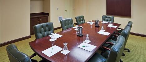 A conference room with a long table, leather chairs, and a wooden cabinet.
