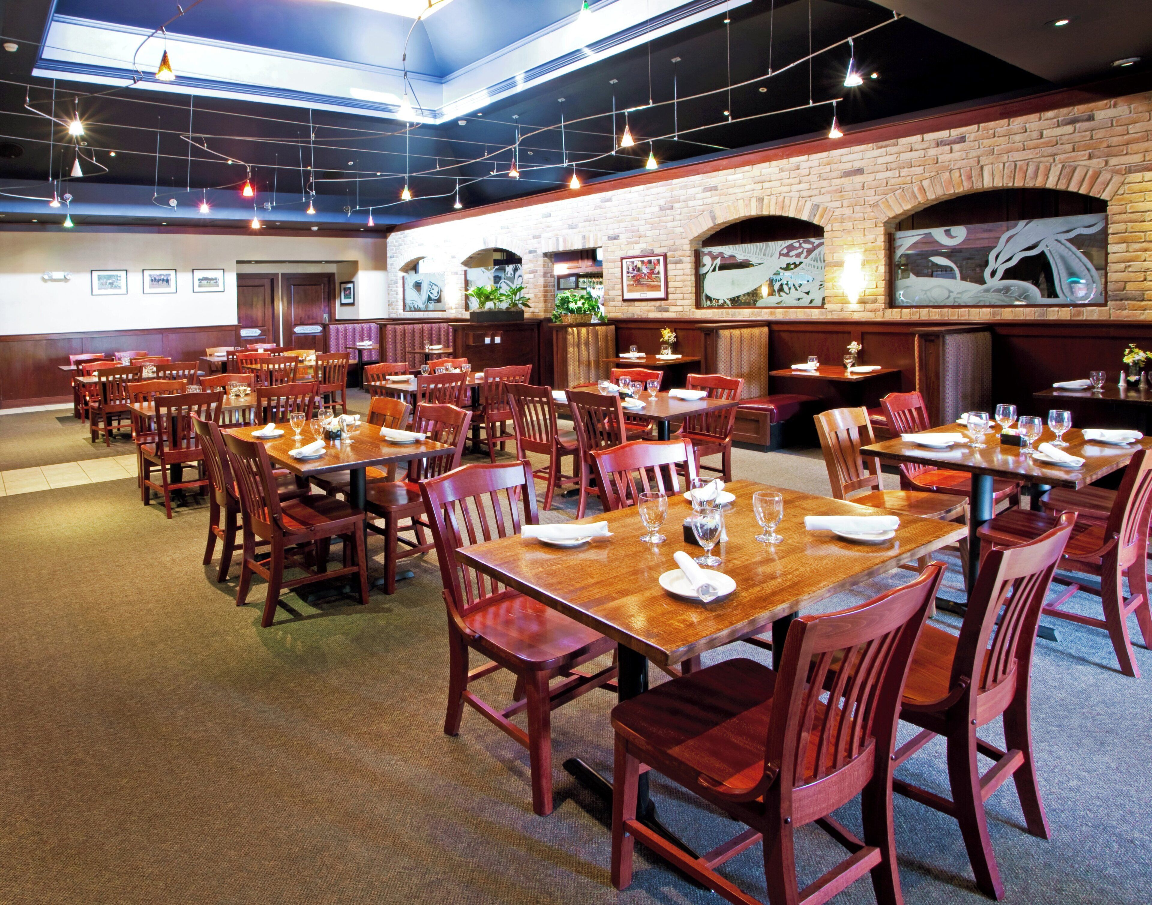A restaurant with multiple tables and chairs, a brick wall, and hanging lights.