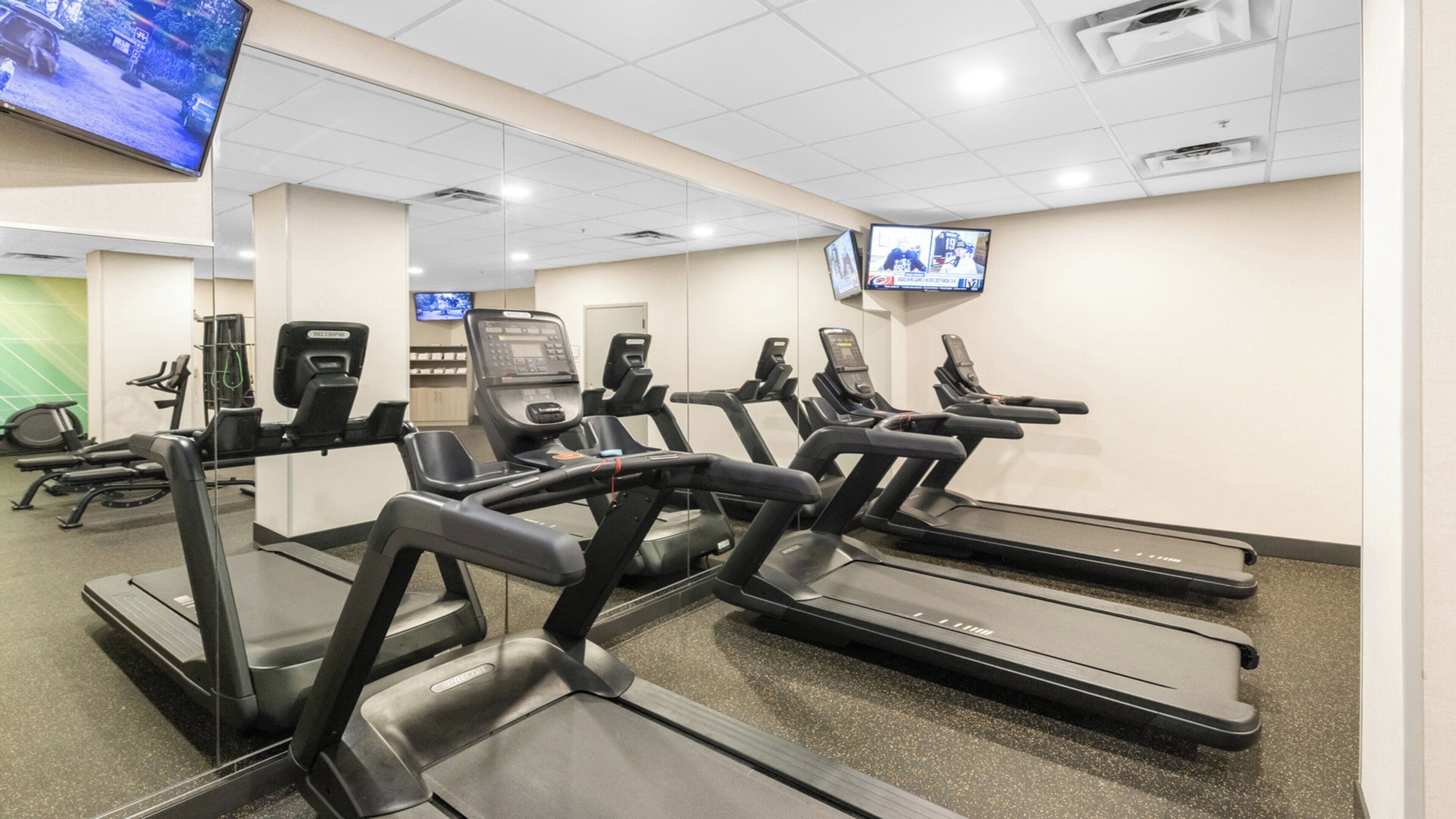 A fitness center with treadmills, exercise bikes, and a television screen on the wall.