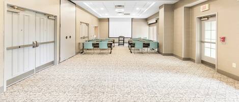 A conference room with tables and chairs, a projector screen, and an exit sign.