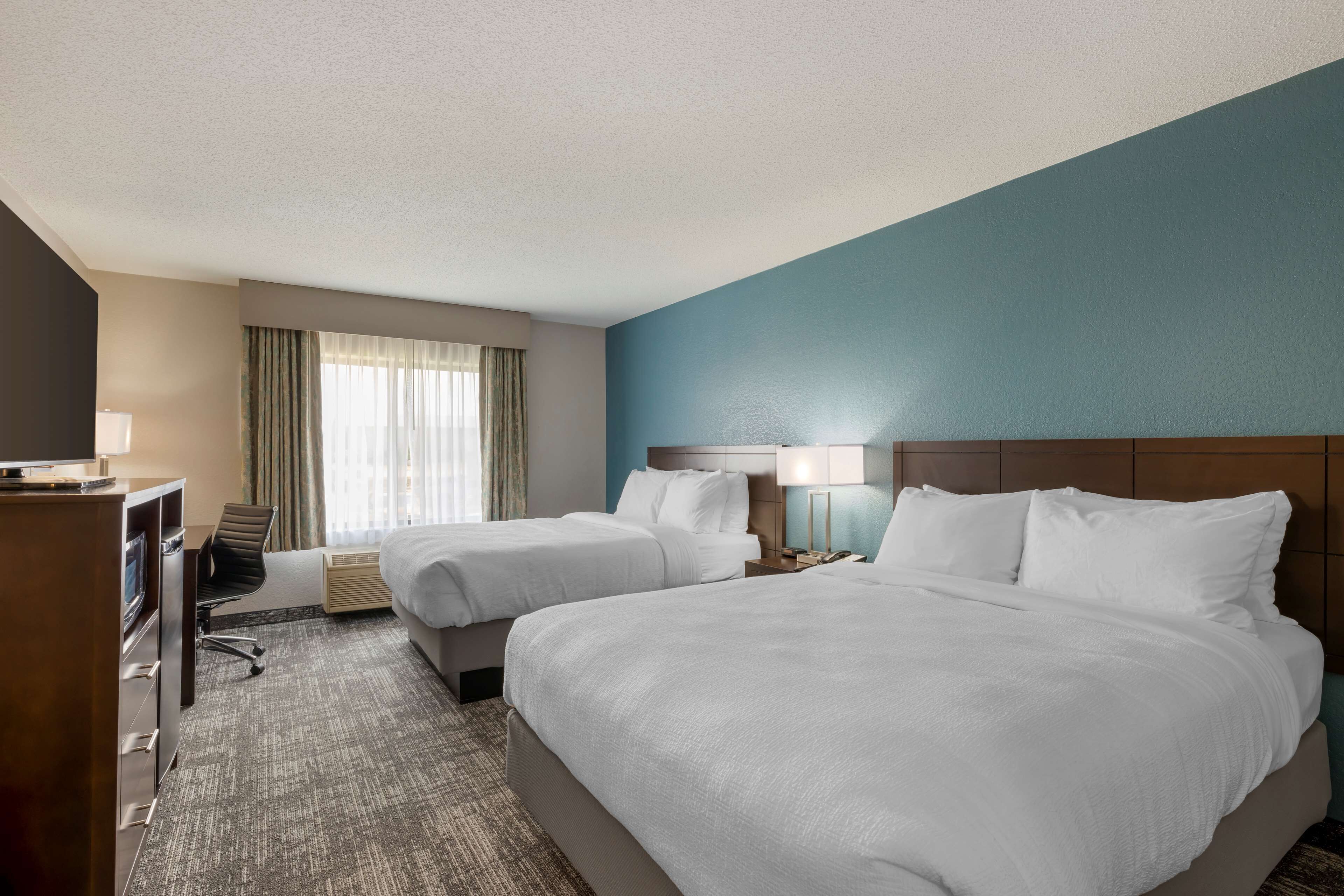 A hotel room with two beds, a desk with a computer, and a chair.