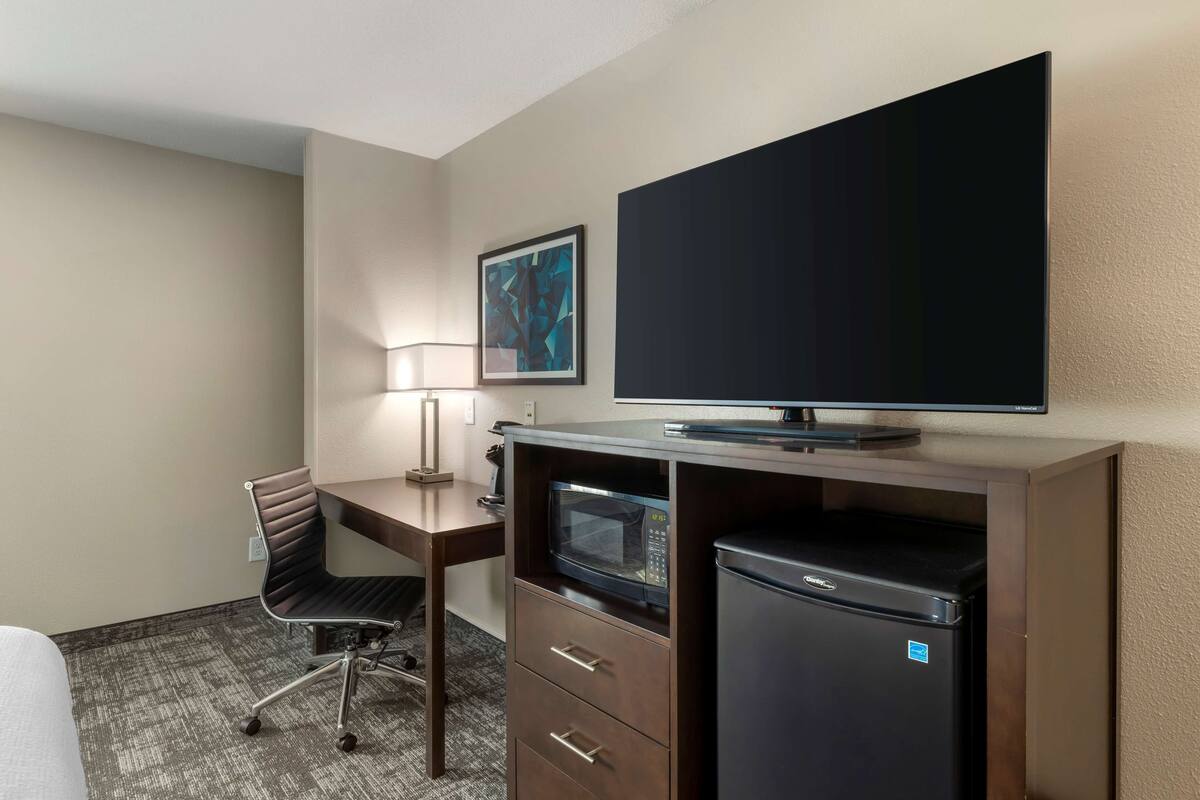 Een hotelkamer met een bed, een bureau met een stoel, een magnetron, een koelkast, een flatscreen-tv en een schilderij aan de muur.