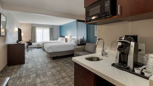 Een hotelkamer met een bed, een bureau, een magnetron, een koffiezetapparaat en een wastafel.
