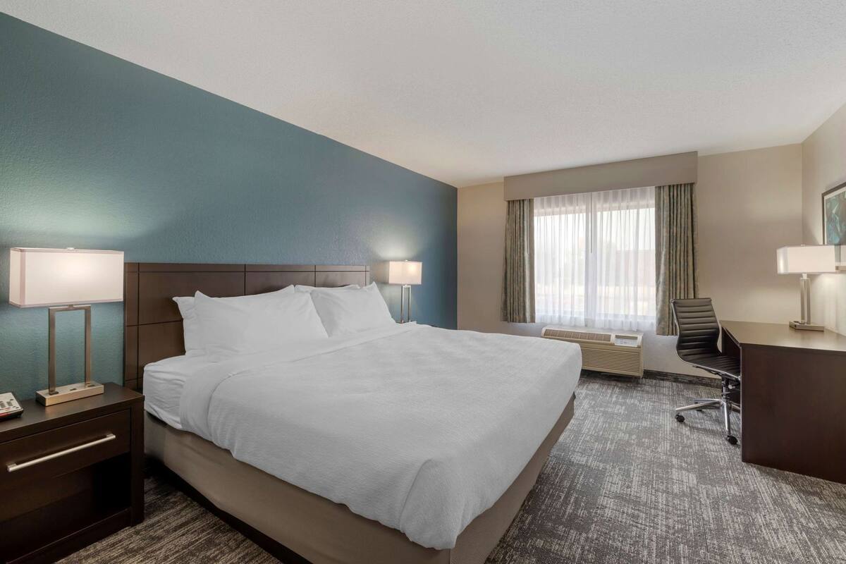 Een hotelkamer met een groot bed, nachtlampjes, een bureau en een stoel.