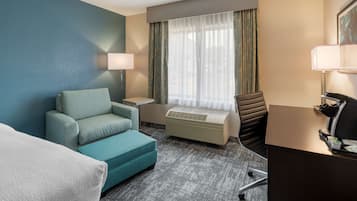 Une chambre d’hôtel équipée d’un canapé, d’un bureau, d’une chaise, d’une lampe et d’une fenêtre avec des rideaux.