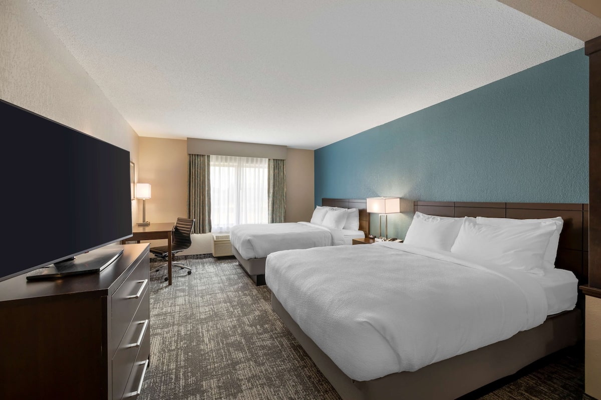 Een hotelkamer met twee bedden, een bureau, een flatscreen televisie, een stoel en een lamp.