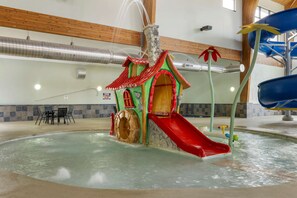 Un espace de jeux aquatiques intérieur comprenant un toboggan, une maison de jeux et une piscine.