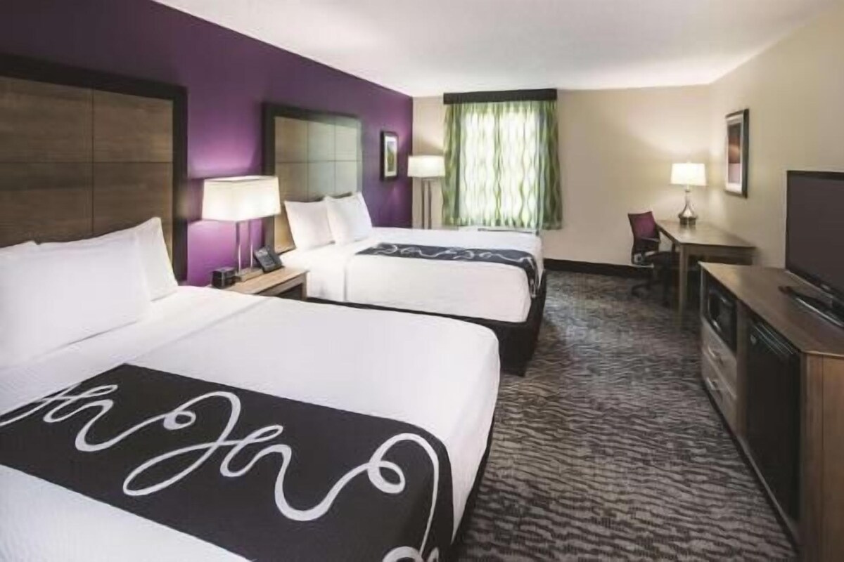 Une chambre d’hôtel avec deux lits, un bureau, une chaise et un téléviseur.
