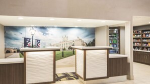 A reception area with a mural of a historic building, a reception desk, and a beverage refrigerator. - La Quinta Inn & Suites by Wyndham Milledgeville (Milledgeville)
