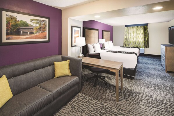 Una habitación de hotel con una cama, un escritorio, un sofá y un cuadro en la pared.