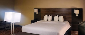 A hotel room with a large bed, two bedside tables, a nightstand, a lamp, and a wall-mounted lamp.