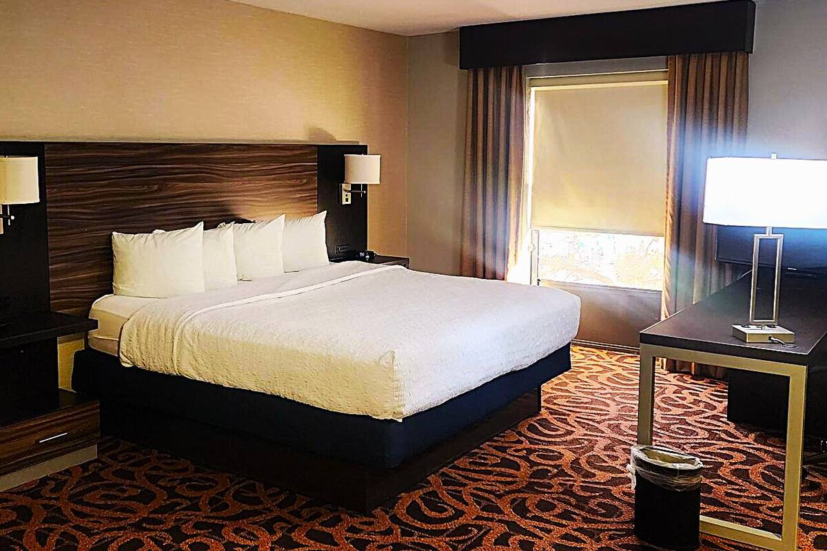 Habitación de hotel con una cama grande, dos mesitas de noche con lámparas, un escritorio con silla y una ventana con cortinas.