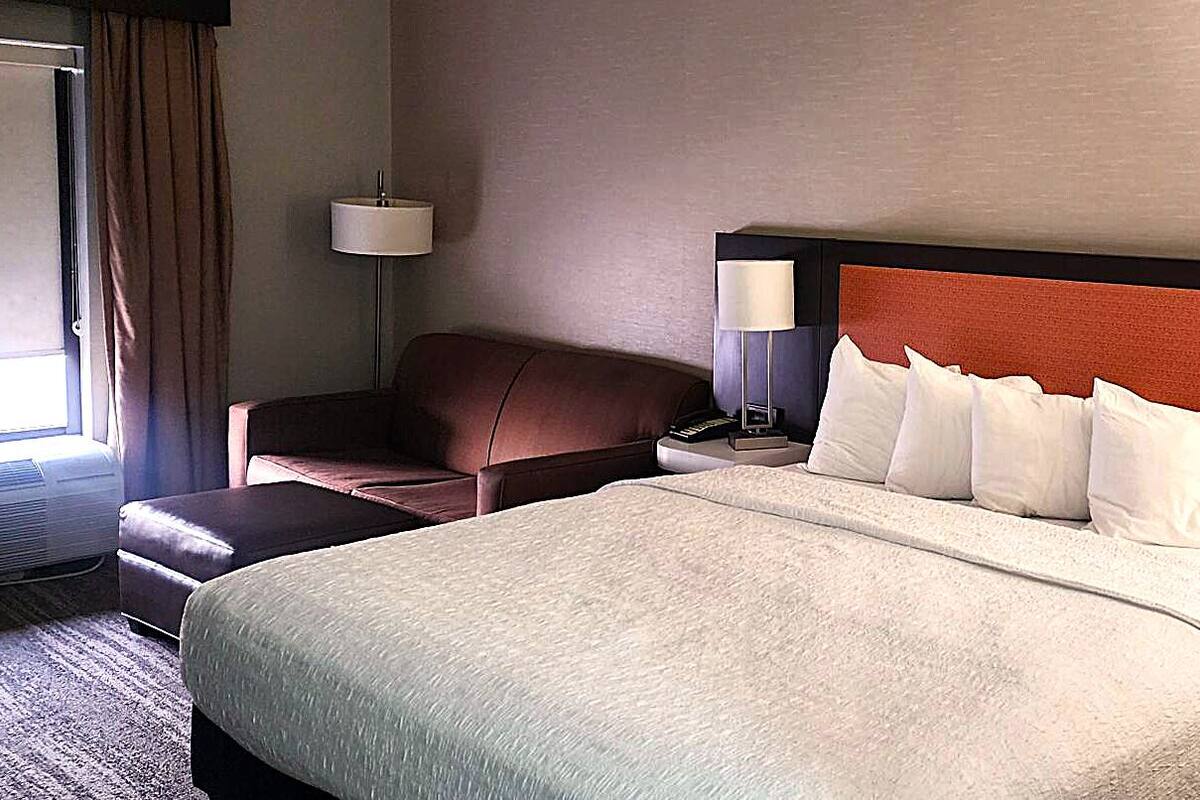 Una habitación de hotel con cama, mesita de noche, lámpara, silla y ventana.