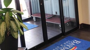 A hotel entrance with an exit sign, a blue mat with 'BAYN' and 'SOUTH' on it, a potted plant, and a cart in the background.