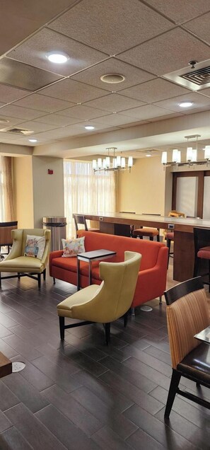 A hotel lobby with a seating area, a reception desk, and a large window with curtains.