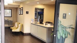 A hotel reception area with a reception desk, chairs, a coffee machine, and a plant.