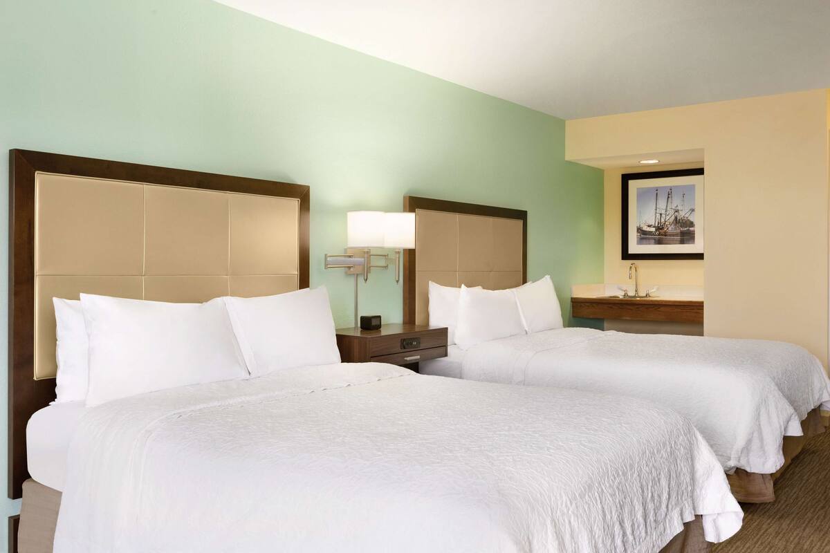 A hotel room with two beds, a nightstand, a lamp, and a framed picture on the wall.
