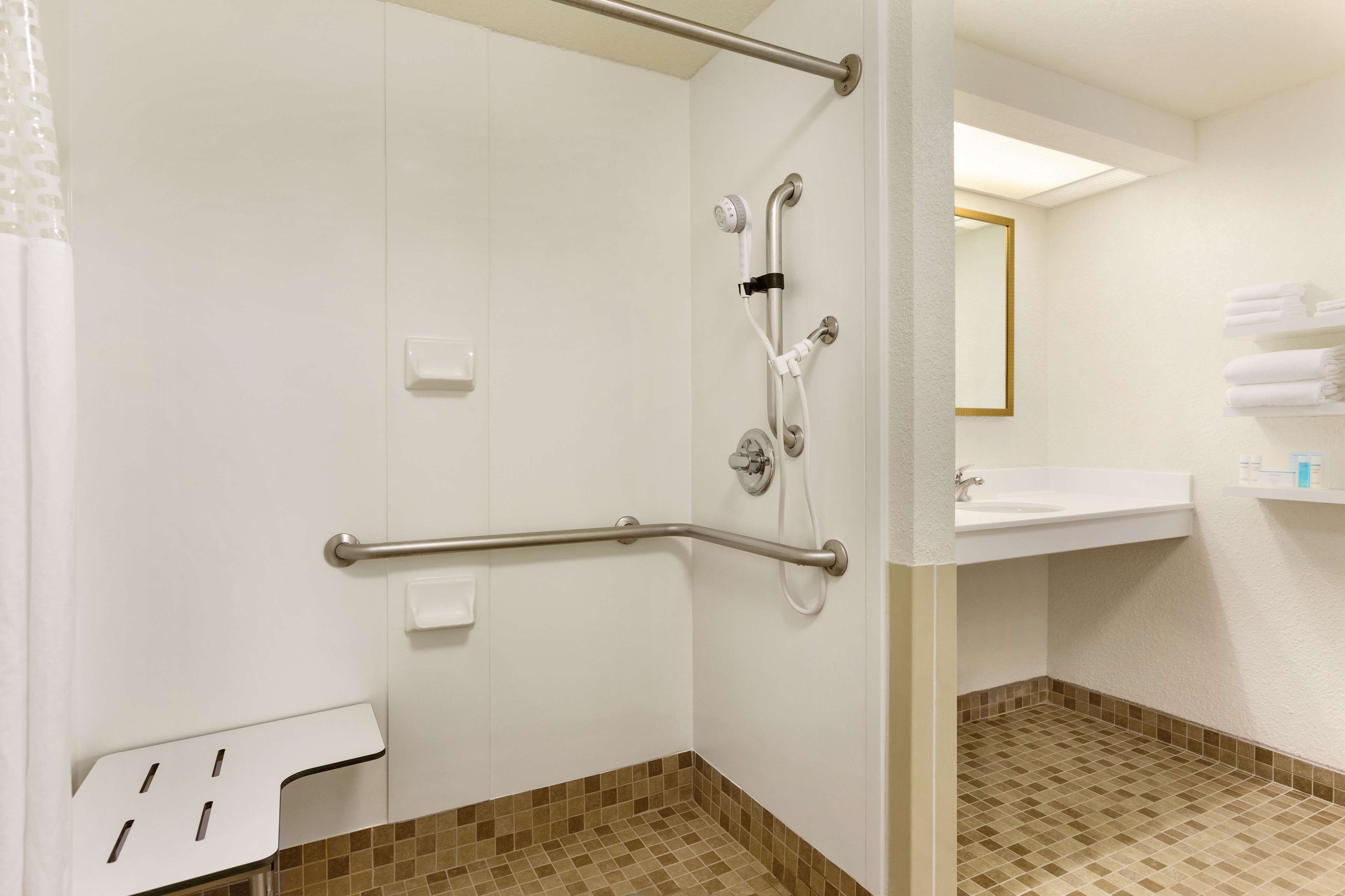 A bathroom with a shower, grab bars, a sink, and a tiled floor.