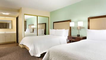 A hotel room with two beds, a large mirror, a bedside table with lamps, and a bathroom with a sink and mirror.