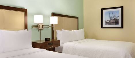 A hotel room with two beds, a nightstand, a lamp, and a framed picture on the wall.