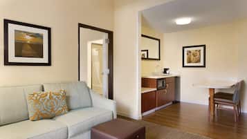 Sala de estar con sofá, una mesa de centro, una mesa de comedor con una silla, zona de cocina y baño visible a través de una puerta abierta.