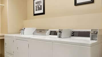 A laundry area with three stacked washers and dryers, a white countertop, and two framed pictures on the wall.