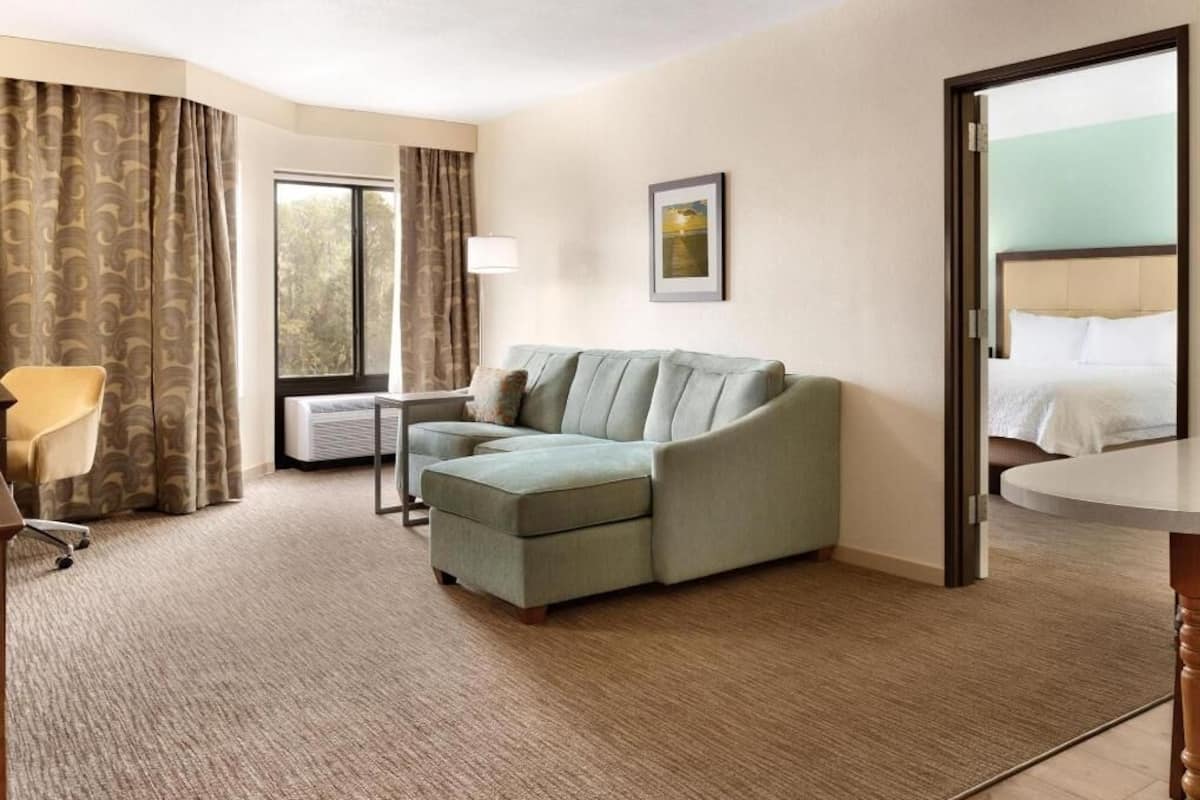 A hotel room with a sofa, a chair, a table, a bed, and a window with curtains.