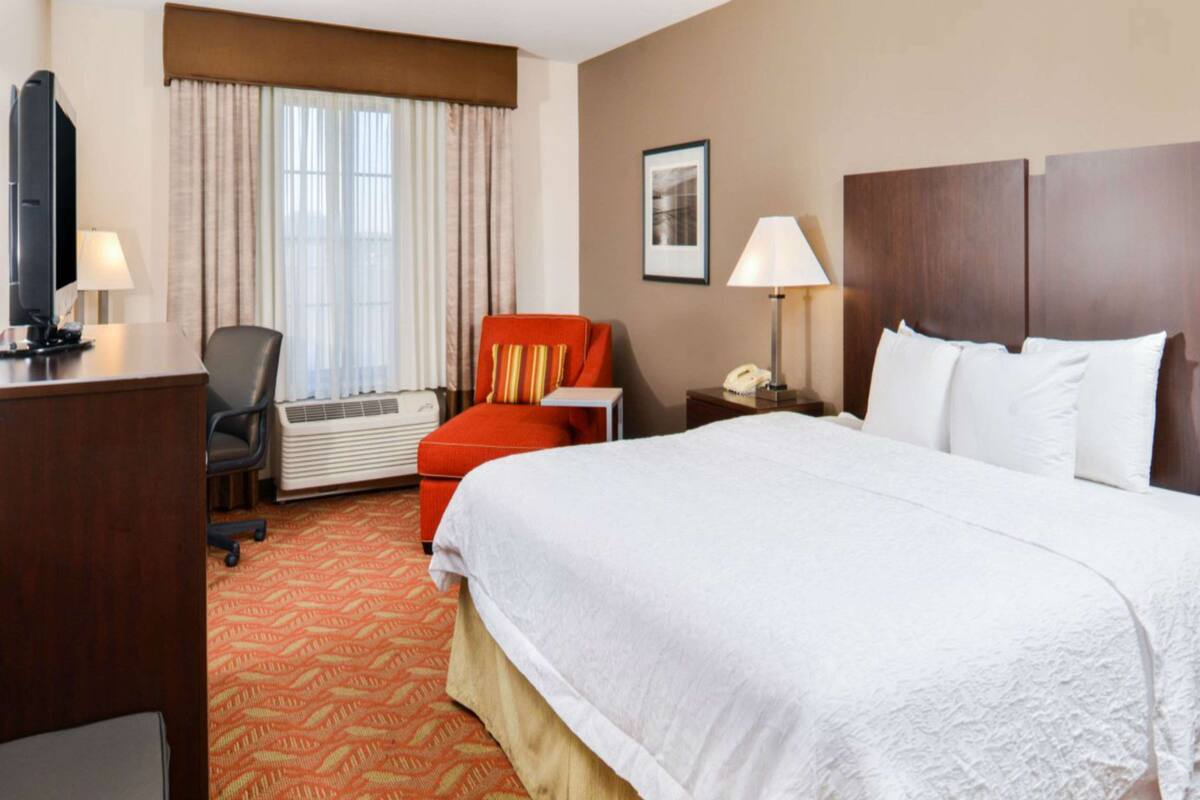 Une chambre d’hôtel avec un grand lit, un bureau avec un ordinateur, une chaise, un appareil de climatisation et une fenêtre avec des rideaux.