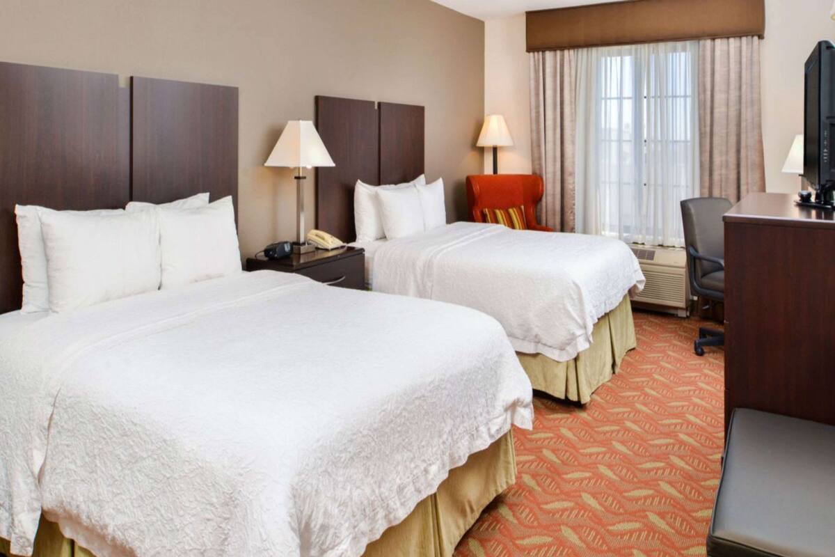 Une chambre d’hôtel avec deux lits, un bureau, une chaise, une télévision et une fenêtre avec des rideaux.
