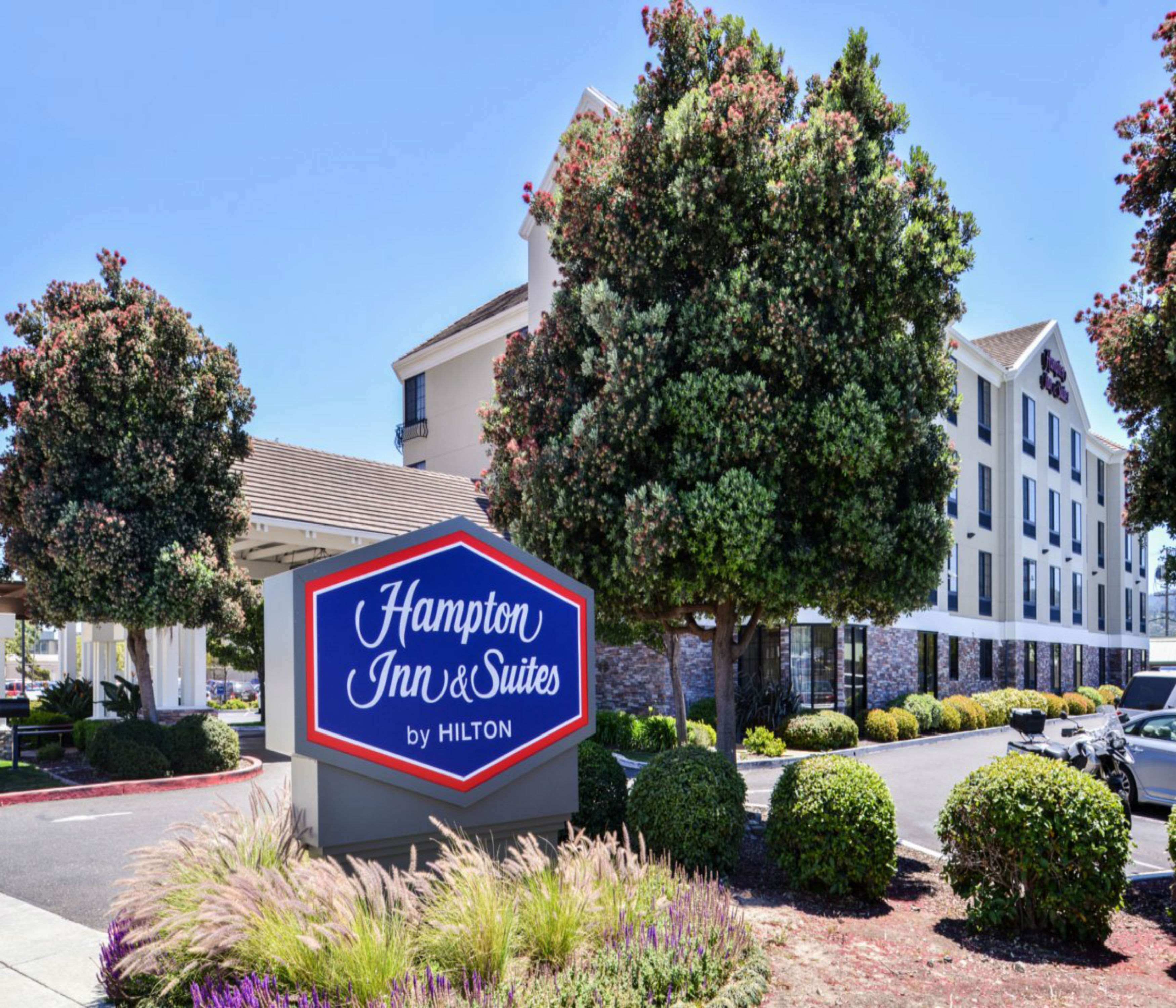 A Hampton Inn & Suites by Hilton sign with a clear view of the building's exterior, including its modern architecture and landscaped surroundings.