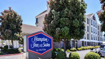 A Hampton Inn & Suites by Hilton sign with a clear view of the building's exterior, including its modern architecture and landscaped surroundings.