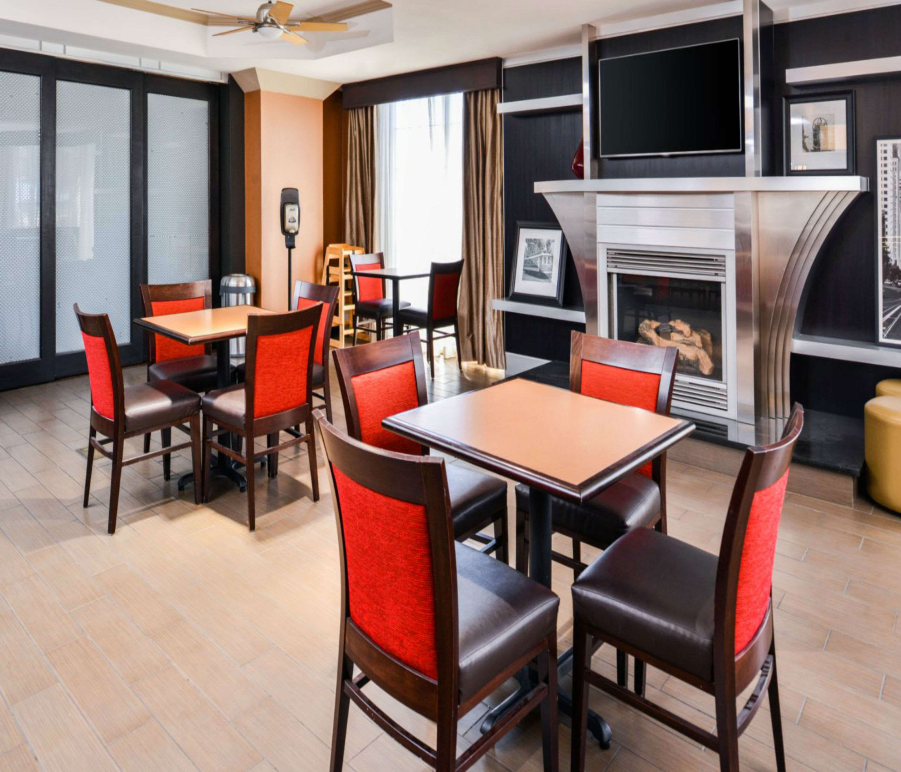 A hotel dining area with wooden tables and chairs, a fireplace, and a television mounted on the wall.