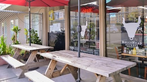 Een buitenzitgedeelte met houten picknicktafels en rode parasols.