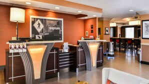 Een hotel receptie met een modern ontwerp, met een receptiebalie, een zithoek met een bank, en een eetgedeelte op de achtergrond.