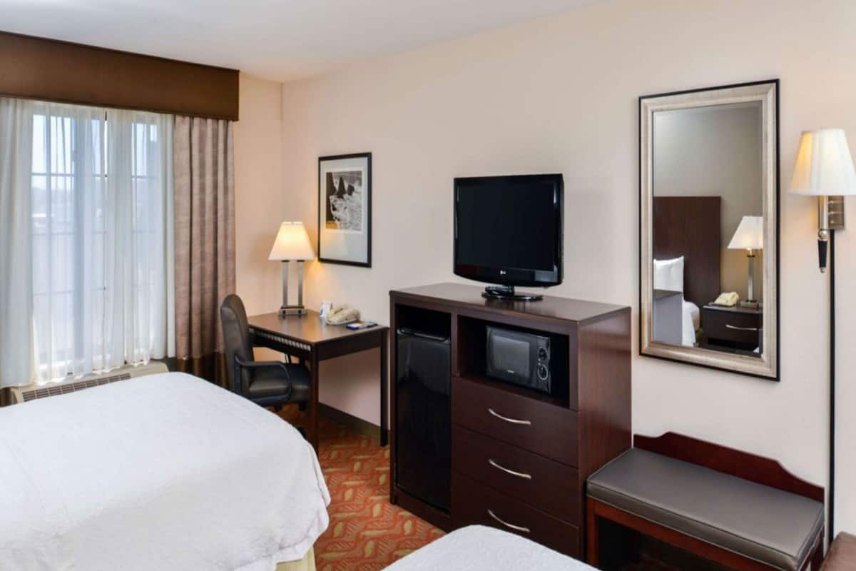Une chambre d’hôtel avec deux lits, un bureau avec une télévision, un miroir et une lampe.