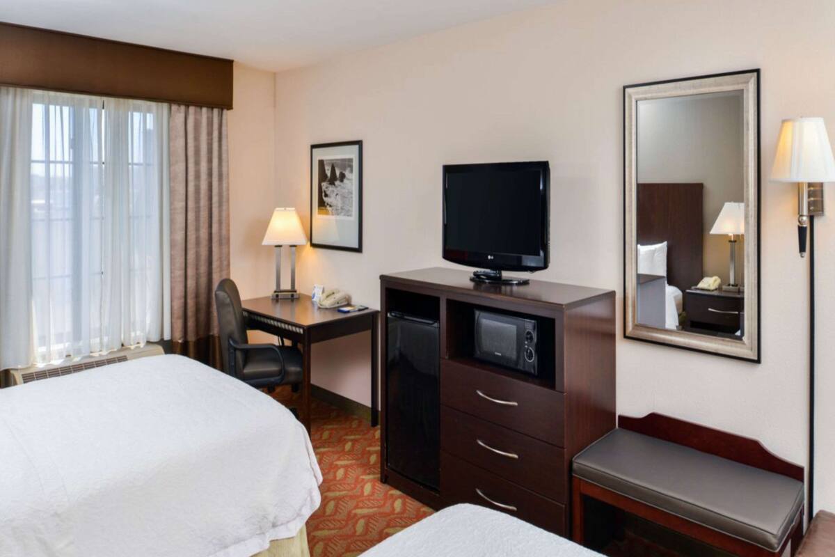 Une chambre d’hôtel avec deux lits, un bureau avec une télévision, un miroir et une lampe.