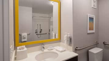 A bathroom with a large mirror, a sink, a toilet, and handrails.