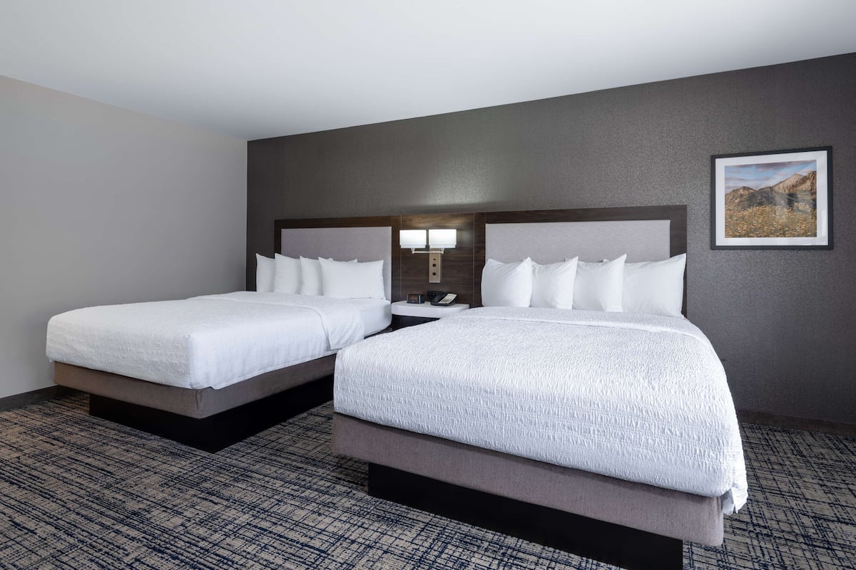 A hotel room with two beds, a nightstand with a lamp, and a framed picture on the wall.