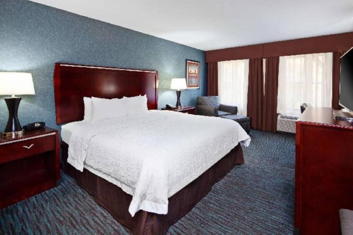 A hotel room with a large bed, a desk, a chair, a TV, and a window with curtains.
