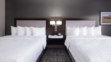 A hotel room with two beds, a nightstand with a lamp, and a framed picture on the wall.