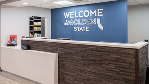 Ein Empfangsschalter mit einem Schild, auf dem 'Welcome to the Golden State' steht, einer Holzpaneel-Gestaltung und dem Hilton-Logo.